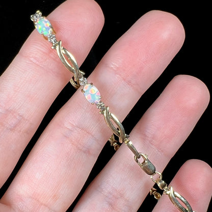 Lab-created opal and diamond tennis bracelet with yellow gold modernist links and lobster clasp shown stretched over top of fingers.