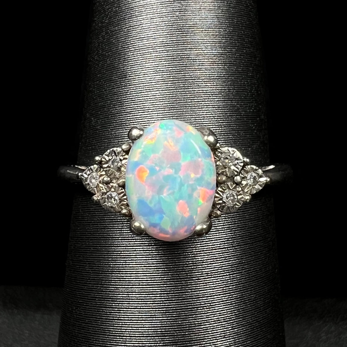 Close-up of estate sterling silver ring mounted with lab-created opal center stone and illusion-set diamond accents, shown on ring display.
