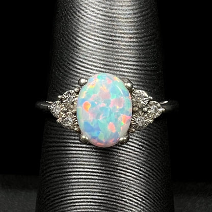 Close-up of estate sterling silver ring mounted with lab-created opal center stone and illusion-set diamond accents, shown on ring display.