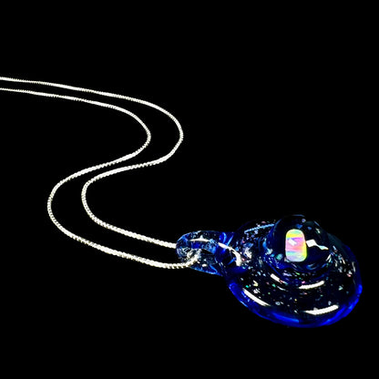 A hand-blown lab opal in blue glass necklace on a silver chain, shown from an angle laying against a black background.