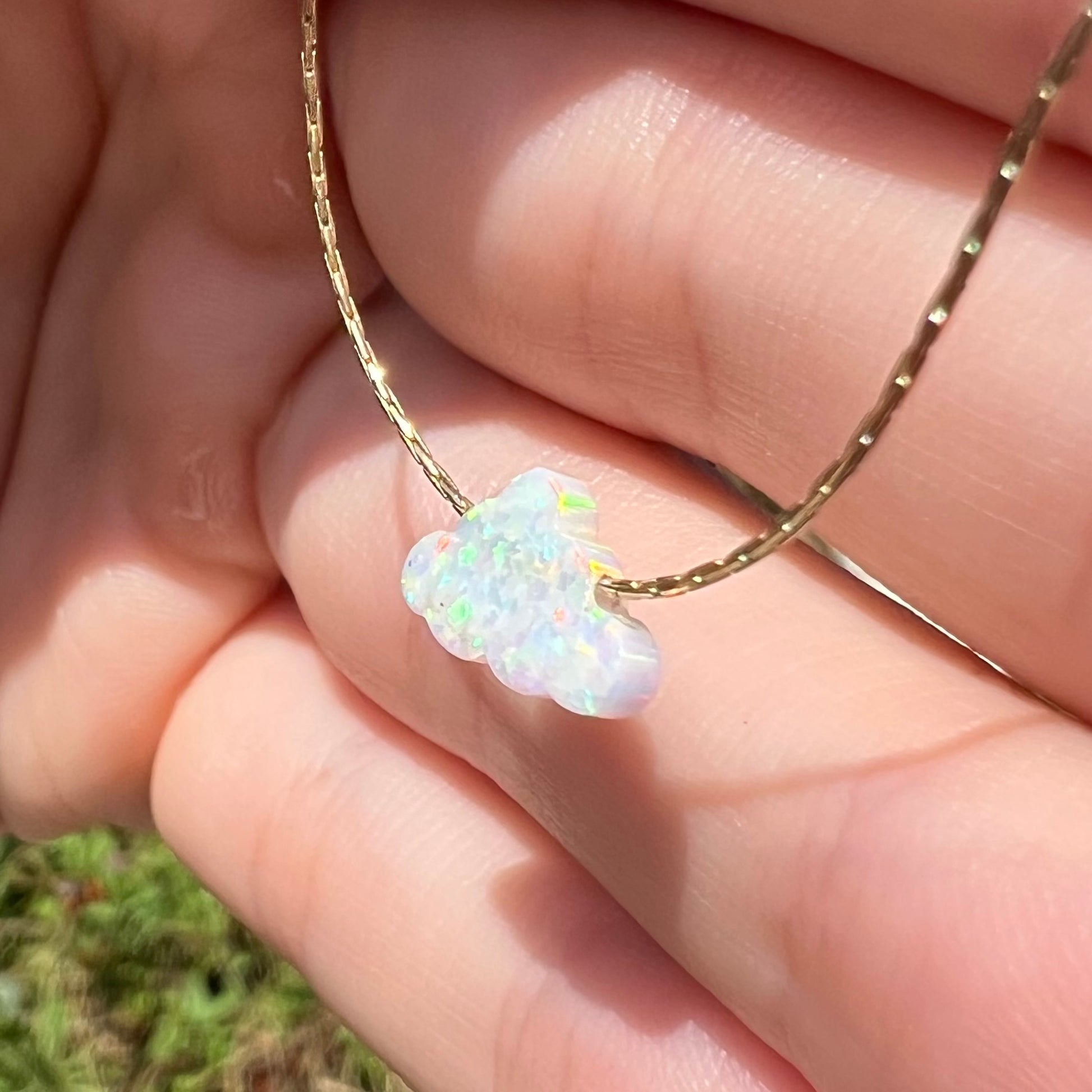 A lab opal cloud necklace held at a sharp angle in daylight.