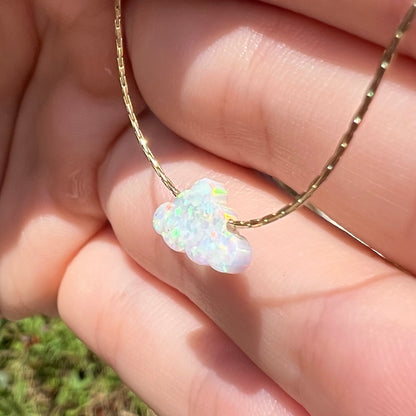 A lab opal cloud necklace held at a sharp angle in daylight.