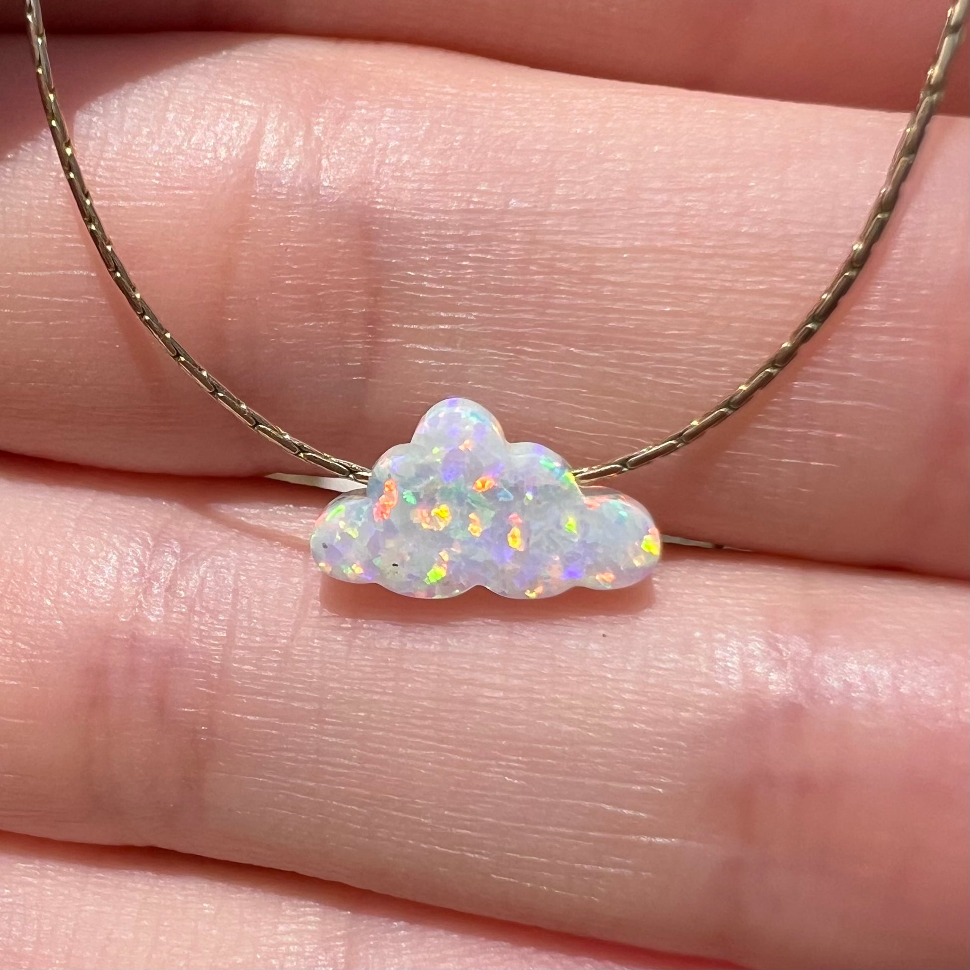Close-up front view of a lab-created opal cloud necklace held by a hand in the sunlight.