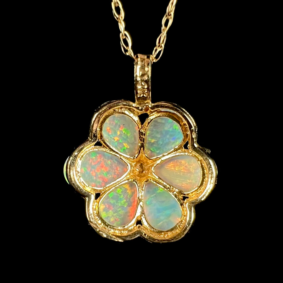 Back side of gold lab-creaed opal flower pendant shown on chain; the pendant's fixed bail has a "14K" hallmark stamp