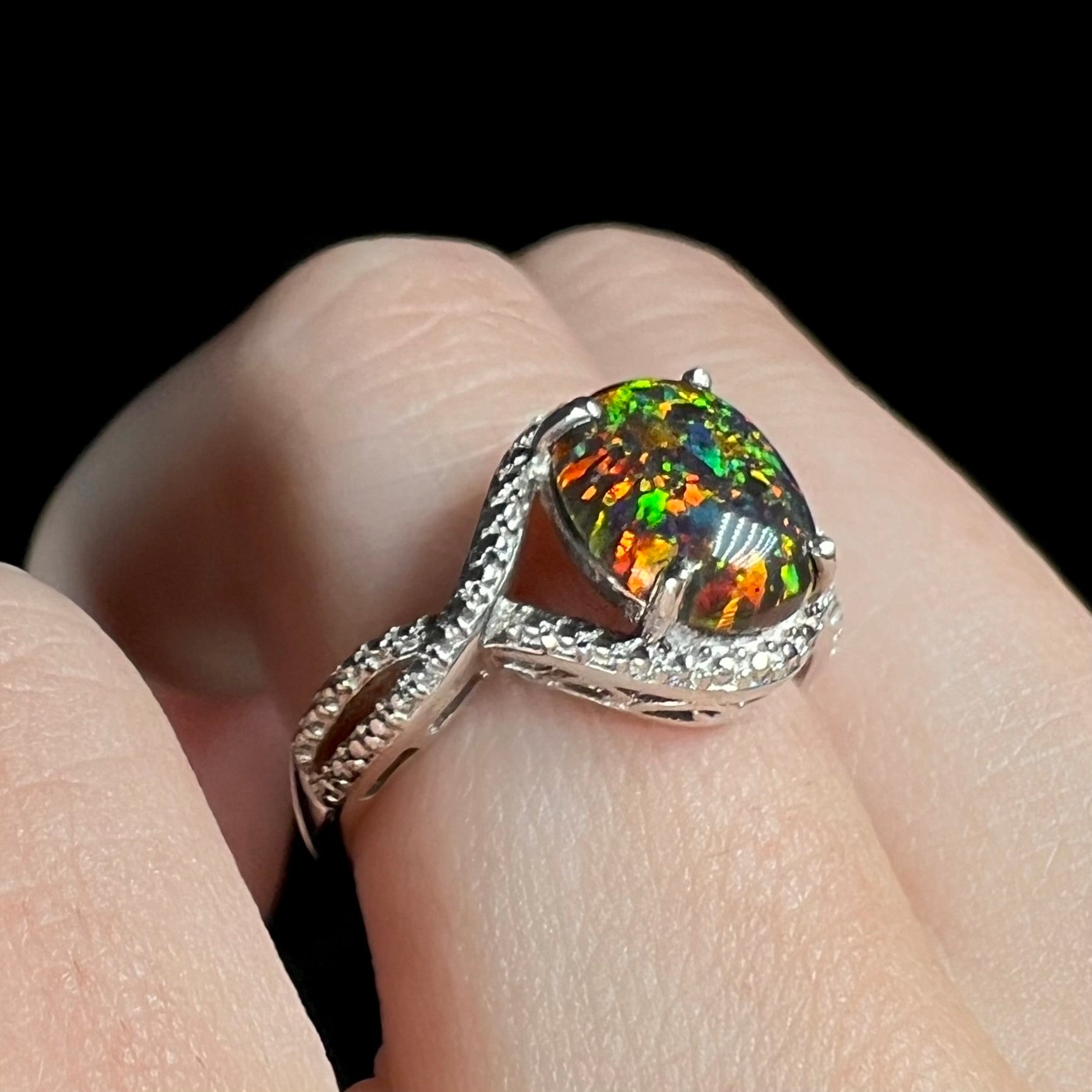 A lab-created black opal solitaire ring with green color play in sterling silver, shown on a hand at an angle.