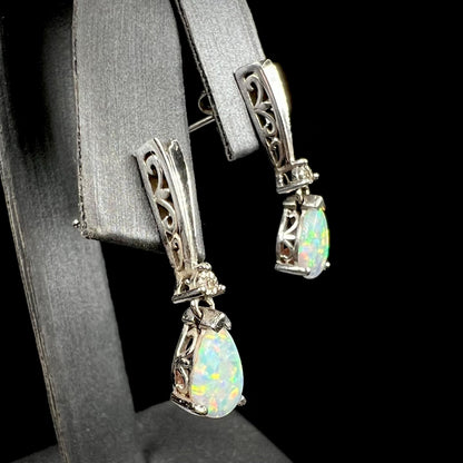 A pair of sterling silver filigree dangle earrings mounted with pear shaped lab created opals and diamond accents.
