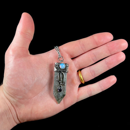 A stainless steal necklace set with a crystal shaped labradorite stone, purple glass, and an opalite accent.