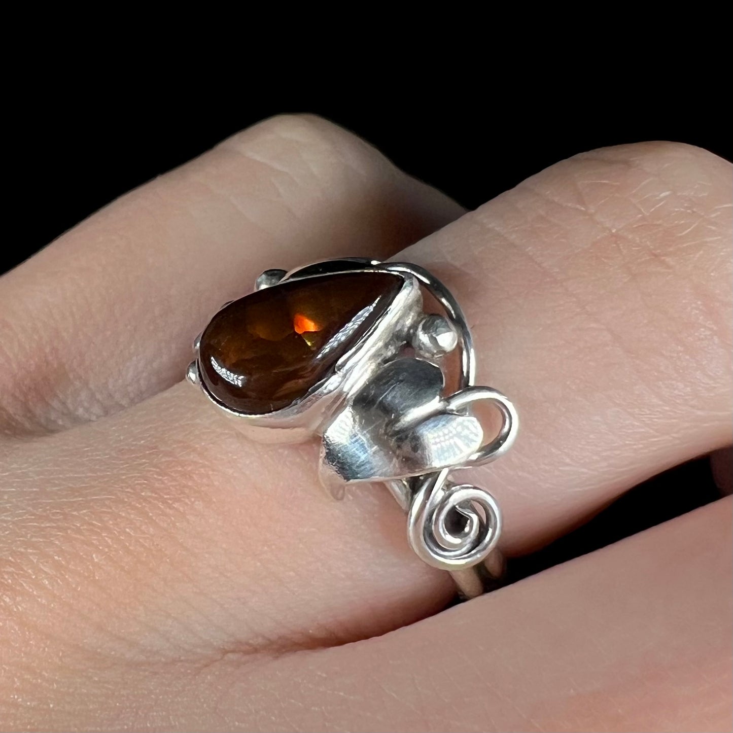 A ladies' pear shaped red fire agate ring with a sterling silver leaf and vine design worn on a finger, shown at an angle.