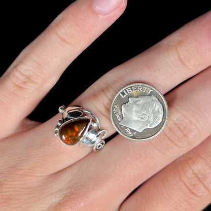 A ladies' pear shaped red fire agate ring with a sterling silver leaf design worn on a hand next to a 1997 S dime coin.