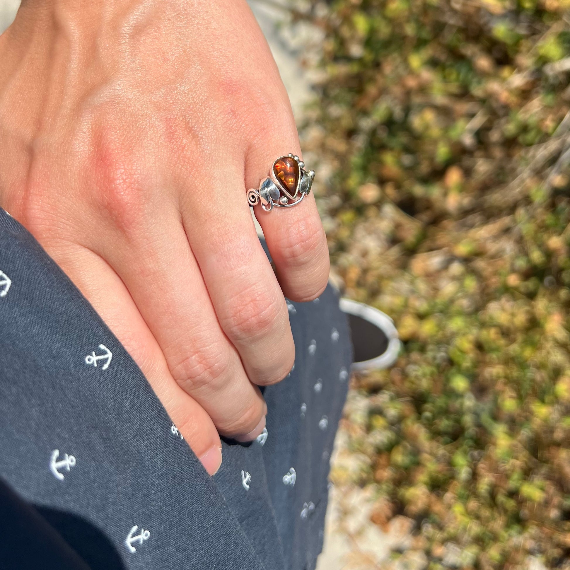 A ladies' pear shaped red fire agate ring with a sterling silver leaf design worn on a hand's pinky finger as it rests on the model's hip.