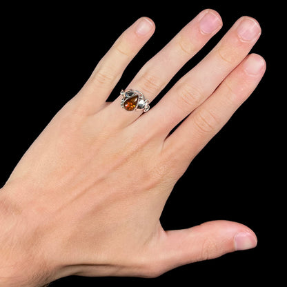 A ladies' pear shaped red fire agate ring with a sterling silver leaf design worn on a hand against a black background.