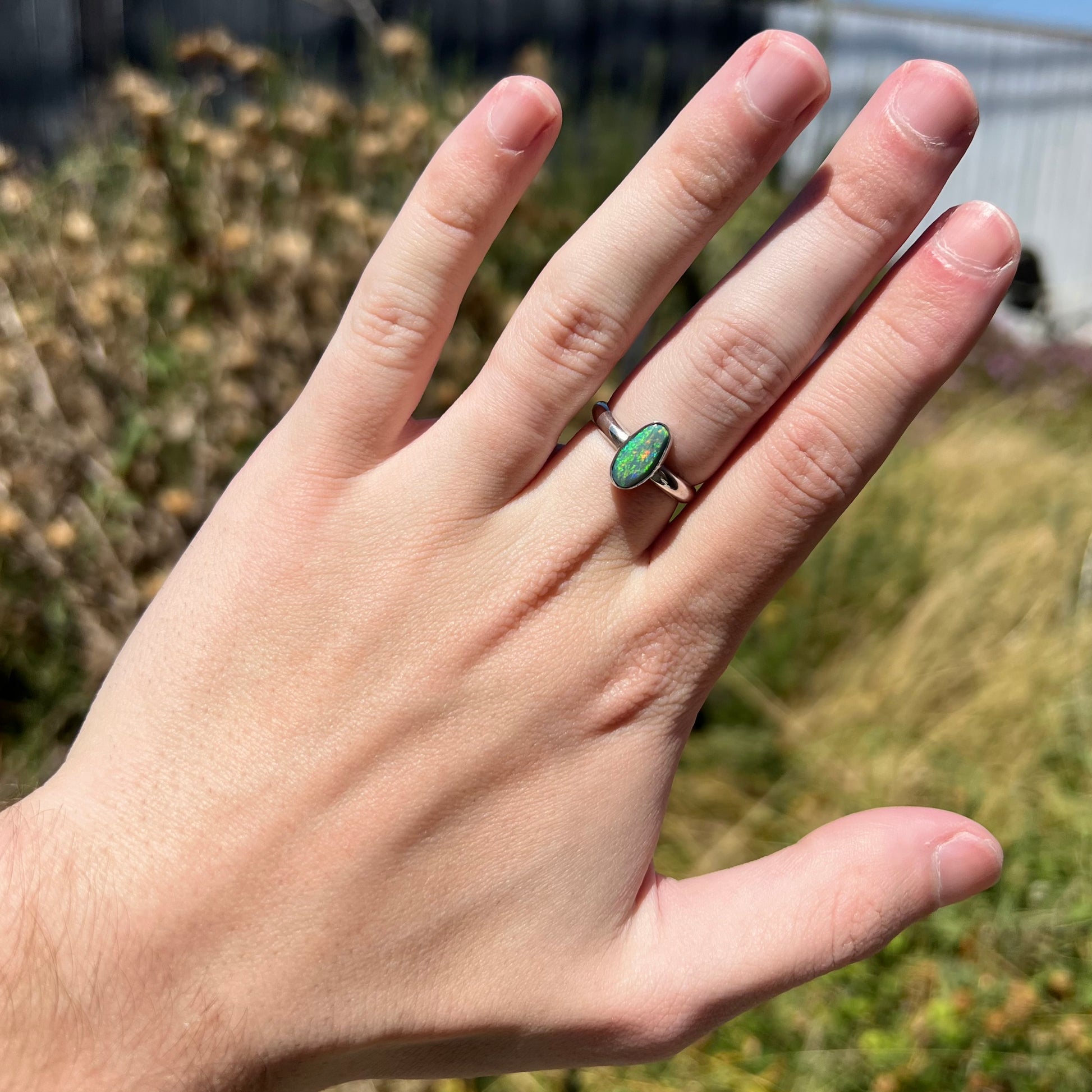 Hand wearing a ladies' Lightning Ridge opal ring in sterling silver.  Green fire is seen in the opal in outdoor sunlight.
