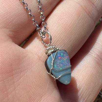A ladies' wire wrapped opal doublet pendant in sterling silver, shown from an angle in natural sunlight.