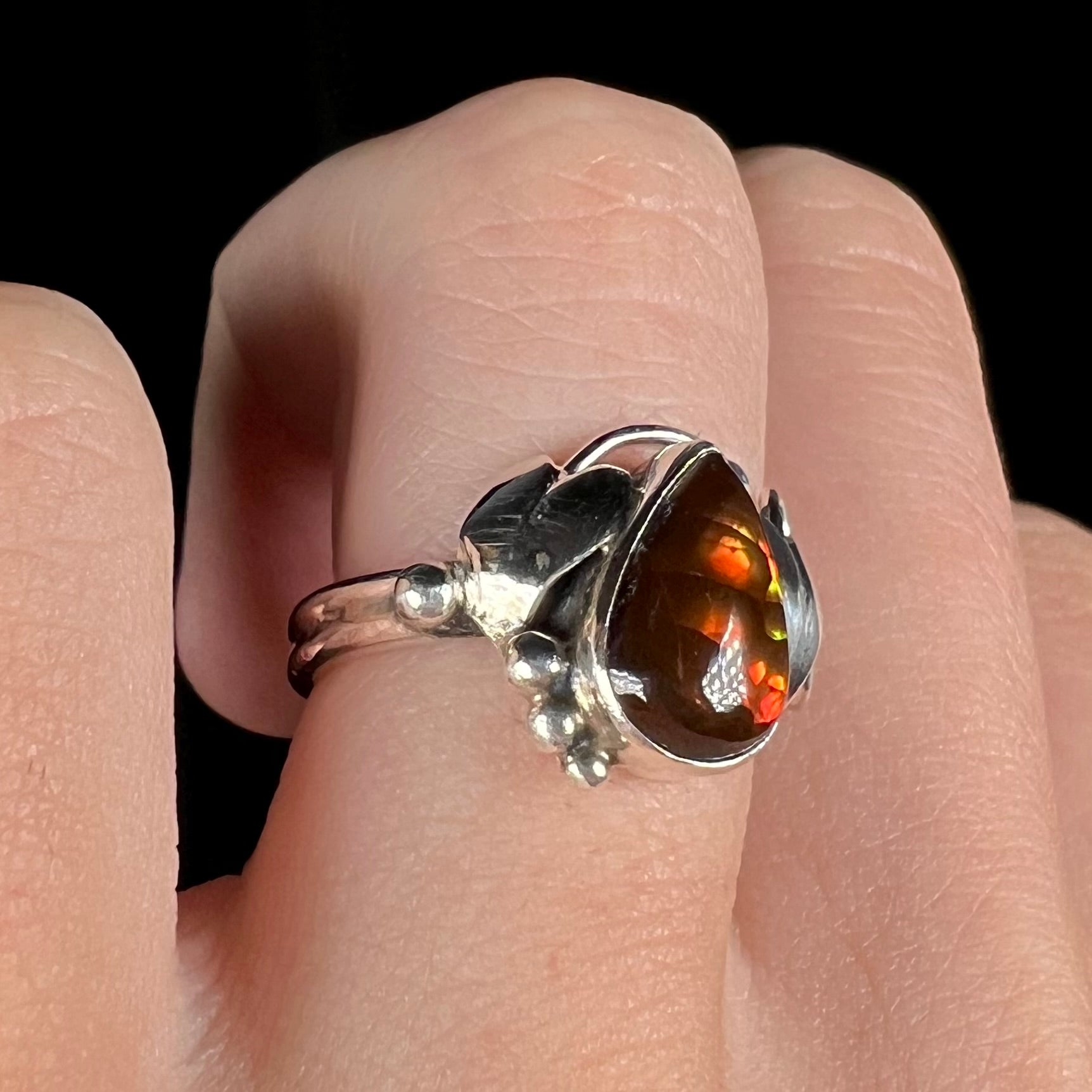 A ladies' pear shaped red fire agate ring with a sterling silver leaf design shown at an angle on a finger.