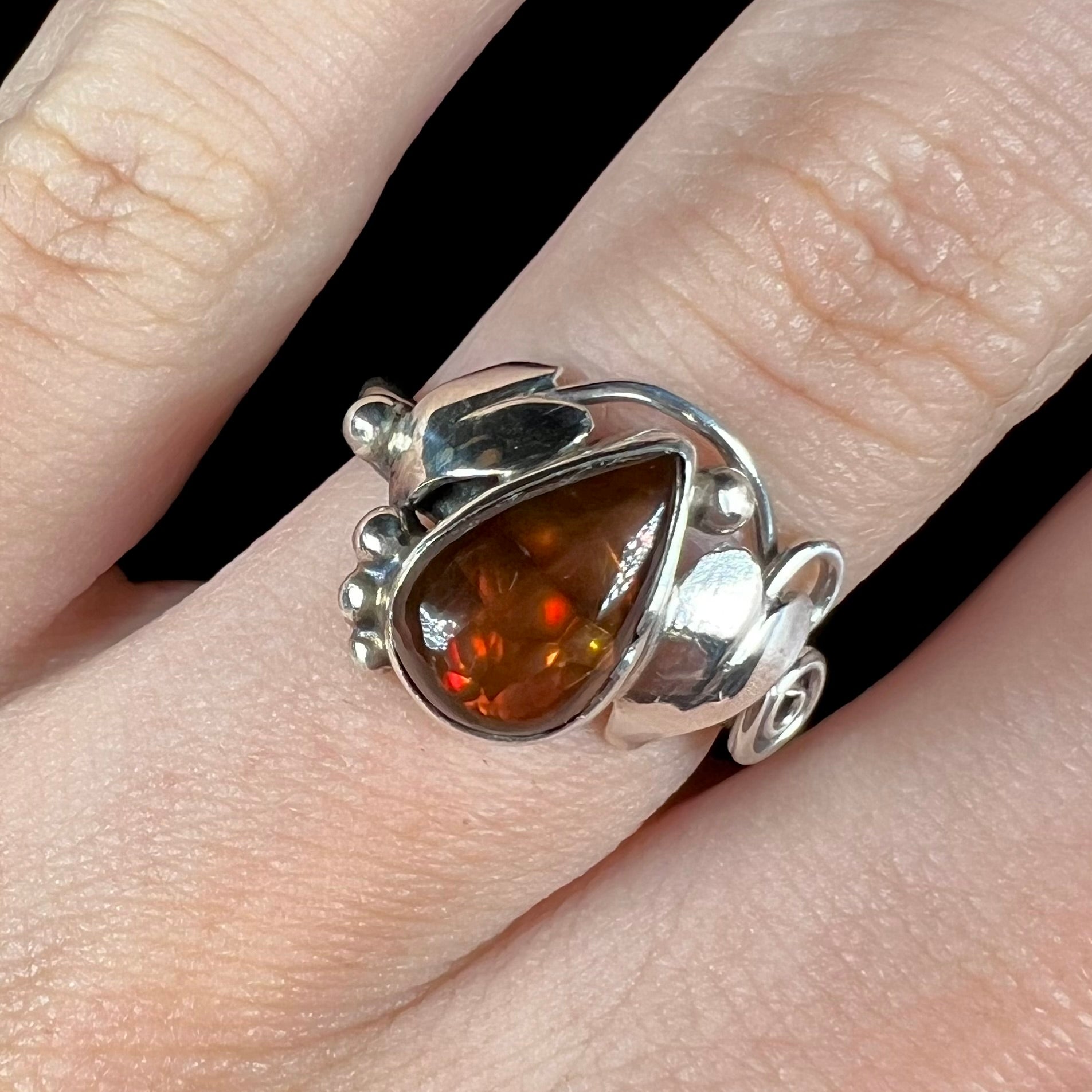 A ladies' pear shaped red fire agate ring with a sterling silver leaf design shown close-up against a black background.