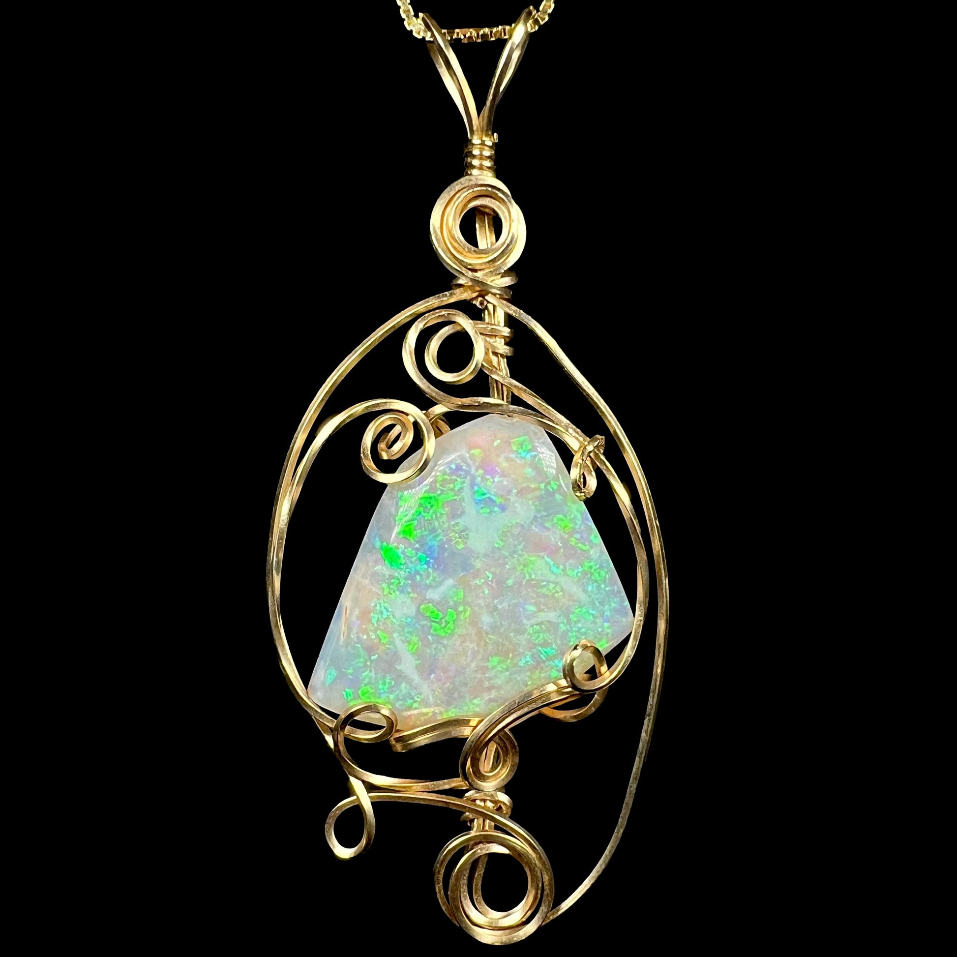 Front close-up of green lambina crystal opal pendant with delicate gold-tone wire wrapped design, shown on chain against black background.