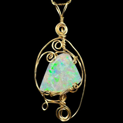 Front close-up of green lambina crystal opal pendant with delicate gold-tone wire wrapped design, shown on chain against black background.