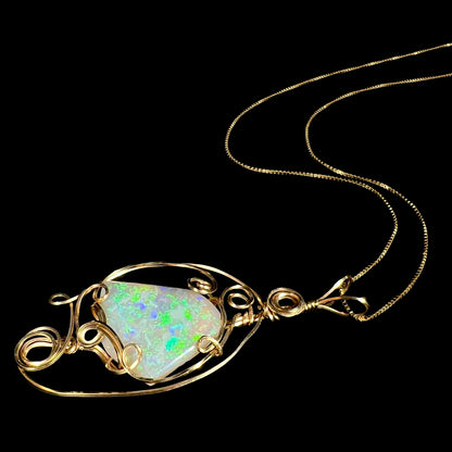 Angled side view of a Lambina opal wire wrapped necklace in gold-tone metal with green play-of-color, laying on a black background with its chain flowing behind the pendant.