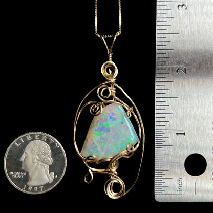 A large wire wrapped opal pendant measuring 2.6 inches in length shown on a chain between a US quarter coin and a ruler for scale.