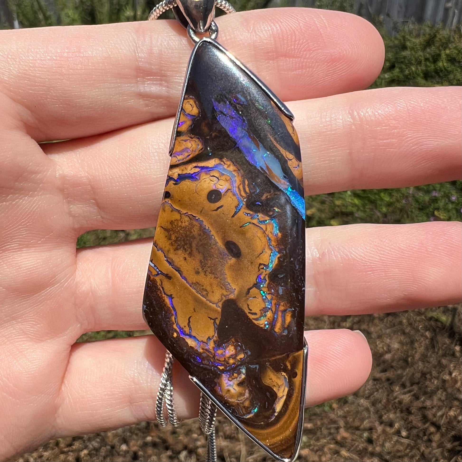 Close-up of large-sized Australian boulder opal pendant with blue, green, and purple veins in sunlight