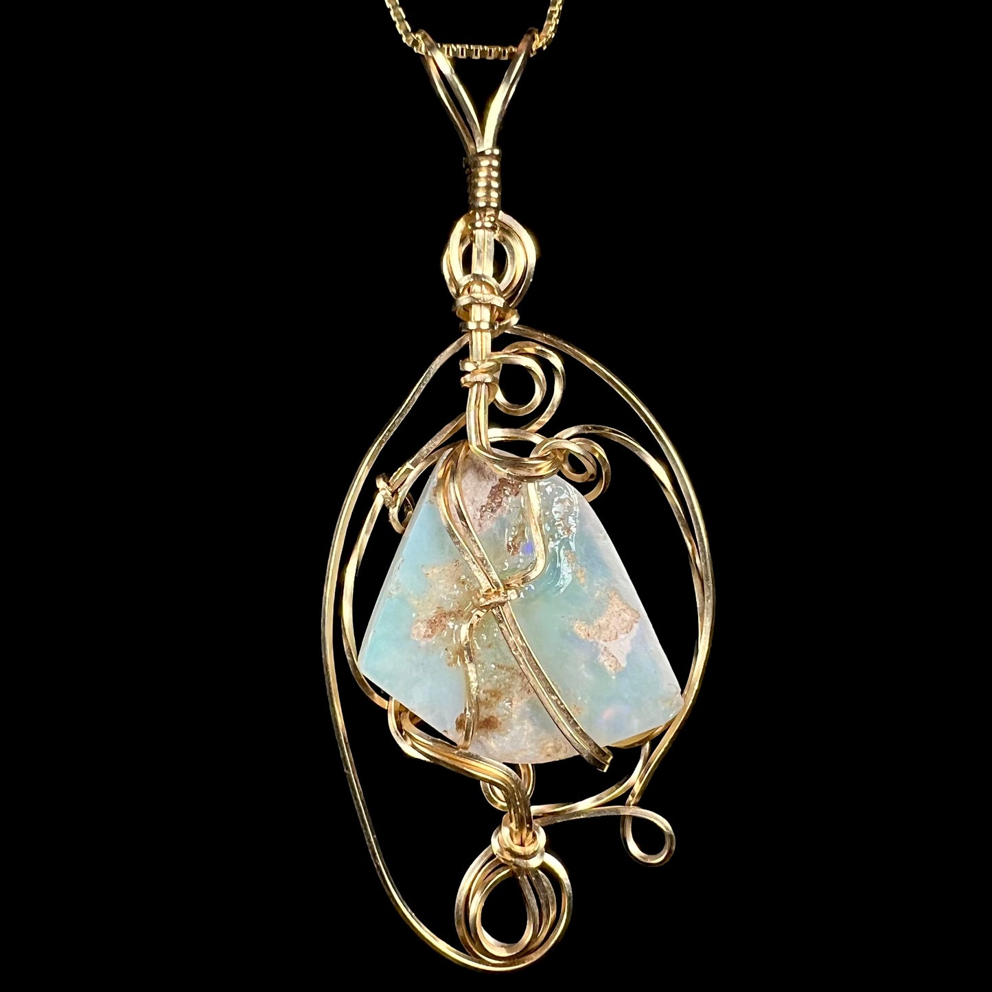 Back side of a gold-tone wire wrapped pendant mounted with a large Australian opal, shown against black background.  The back of the opal has white potch inclusions.