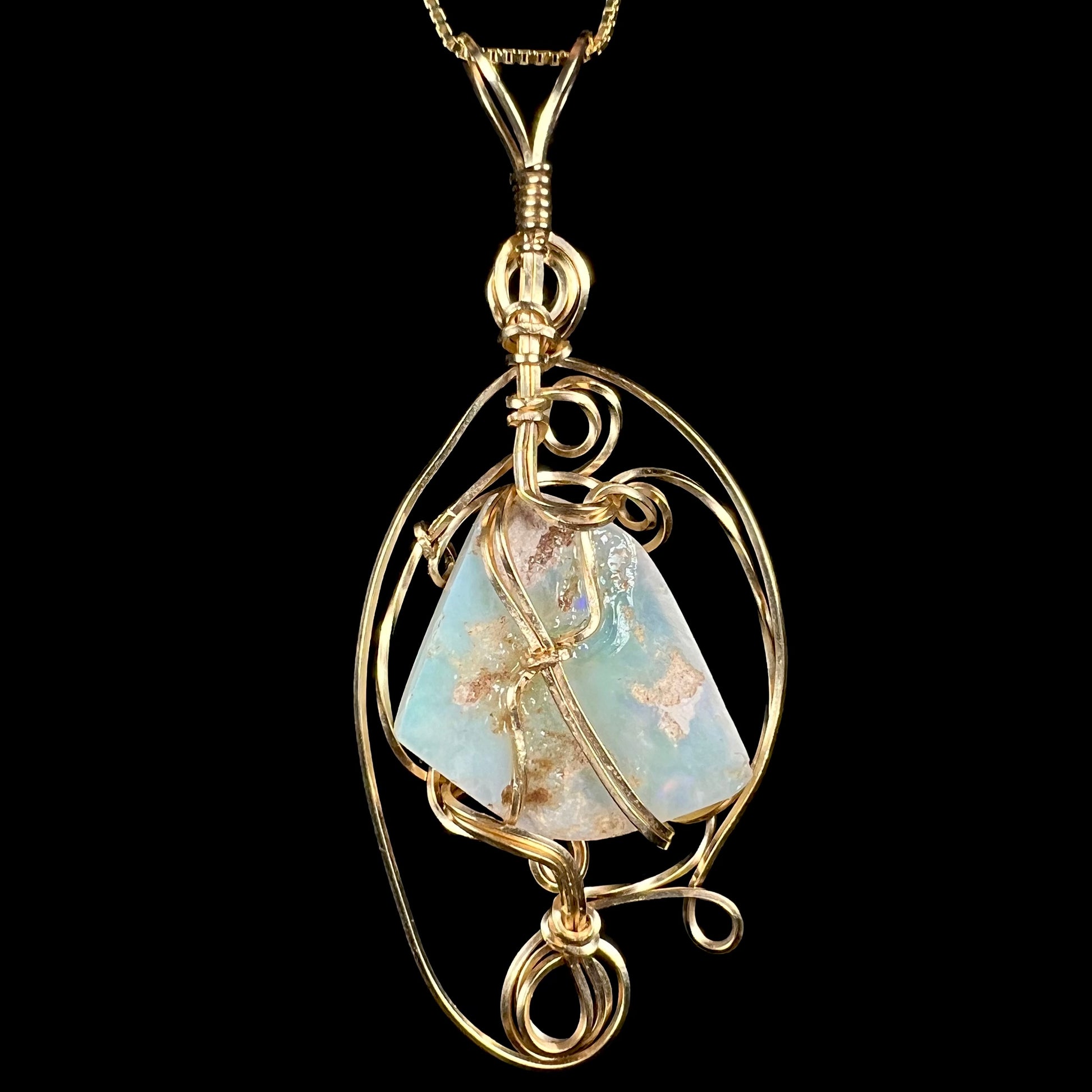 Back side of a gold-tone wire wrapped pendant mounted with a large Australian opal, shown against black background.  The back of the opal has white potch inclusions.