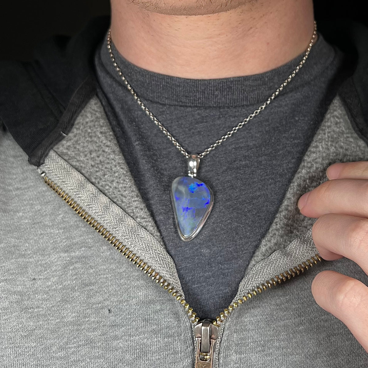 Close-up of man's neck and chest wearing large sterling silver black opal necklace against dark shirt