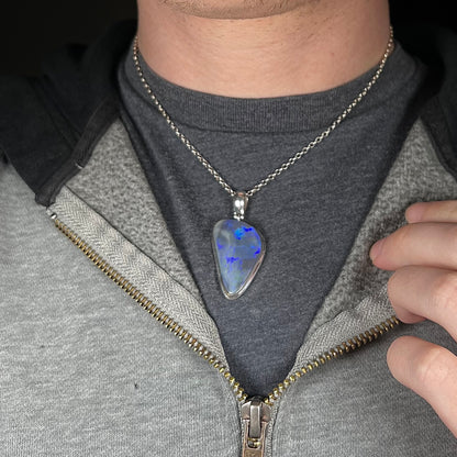 Close-up of man's neck and chest wearing large sterling silver black opal necklace against dark shirt