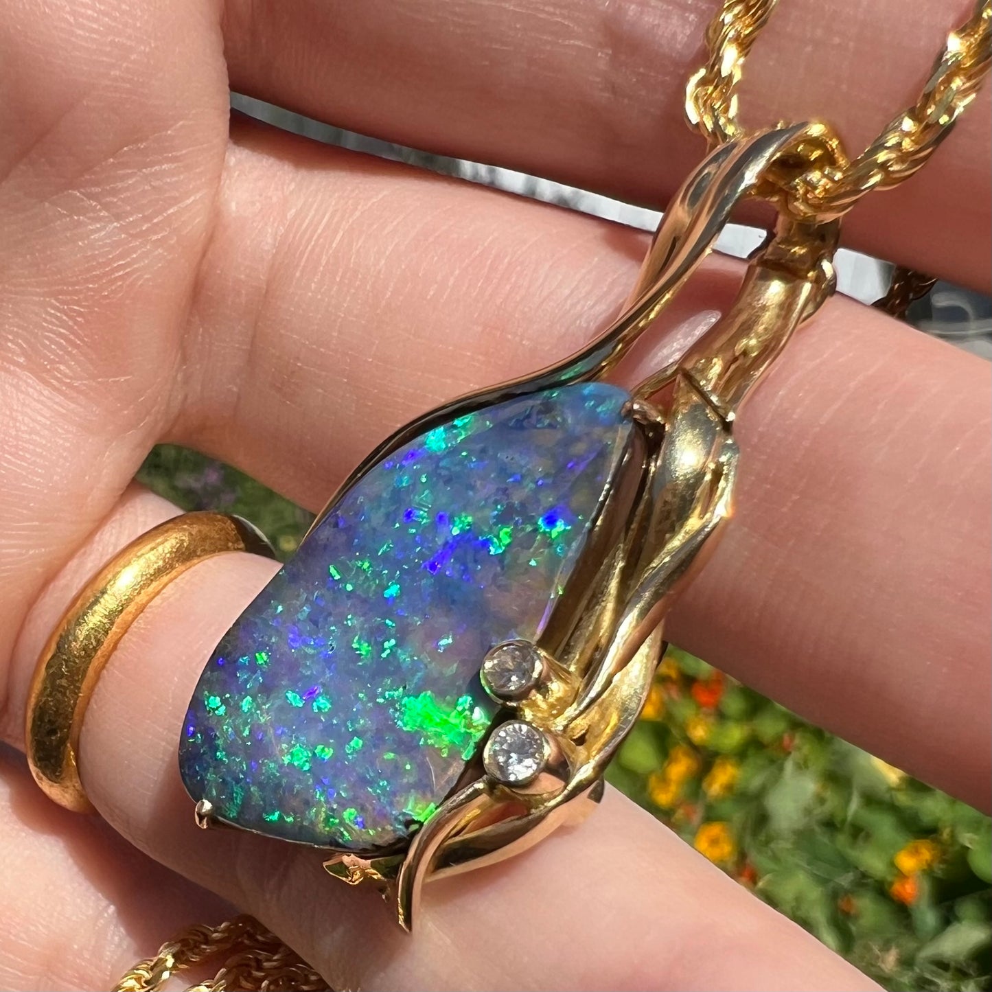 Large Australian boulder opal and diamond statement necklace with green flashes of color, shown in hand from an angle under sunlight.