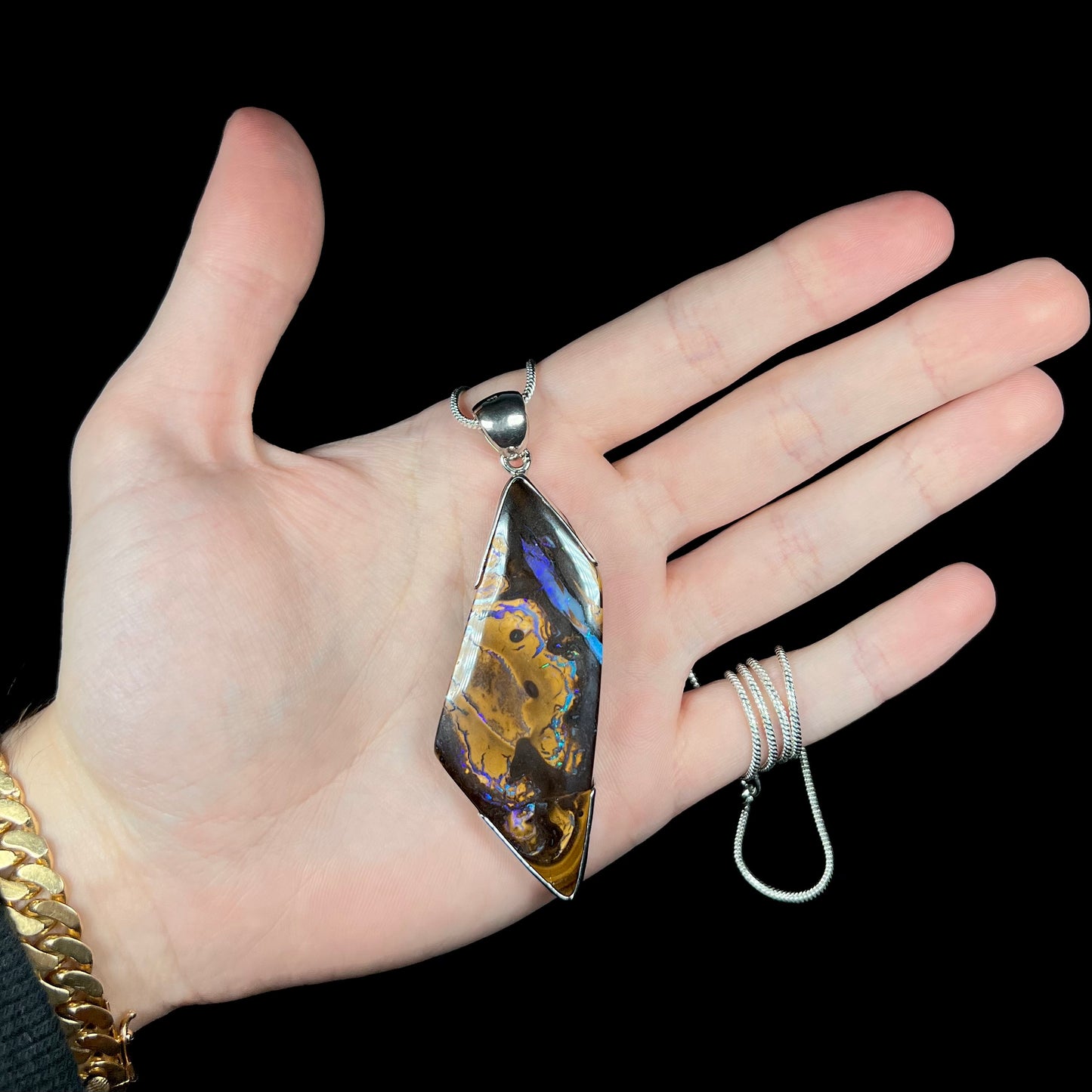 Hand holding large silver boulder opal pendant with chain wrapped around pinky finger