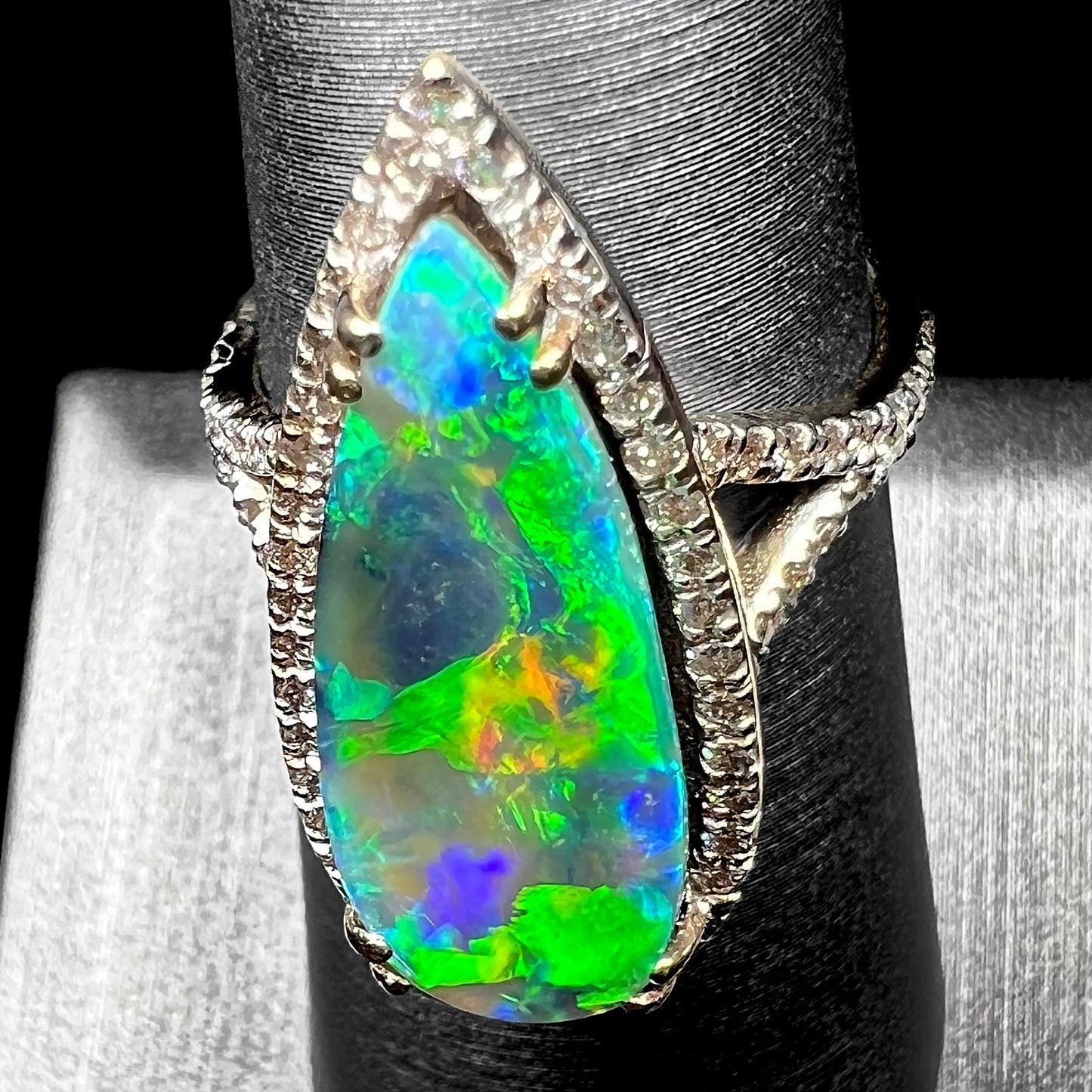 Angled down-facing view of a large green boulder opal engagement ring with a directional green flash of color play, shown on a ring display.