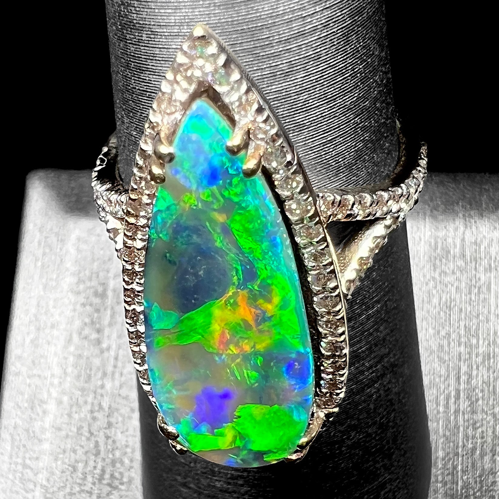 Angled down-facing view of a large green boulder opal engagement ring with a directional green flash of color play, shown on a ring display.