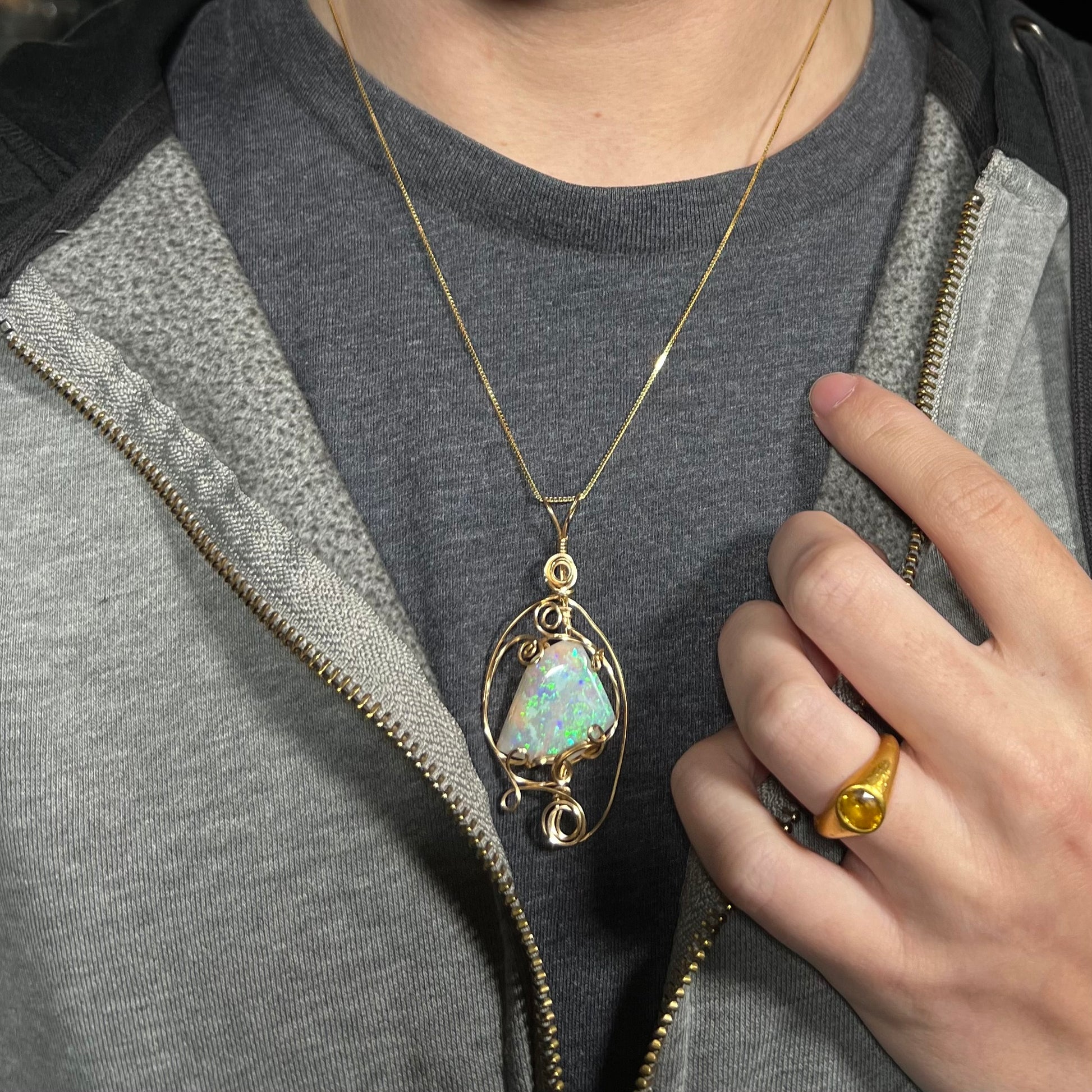 Close-up of person wearing a large Lambina opal necklace with a gold-tone wire wrapped design around their neck against a dark shirt beneath a hoodie.
