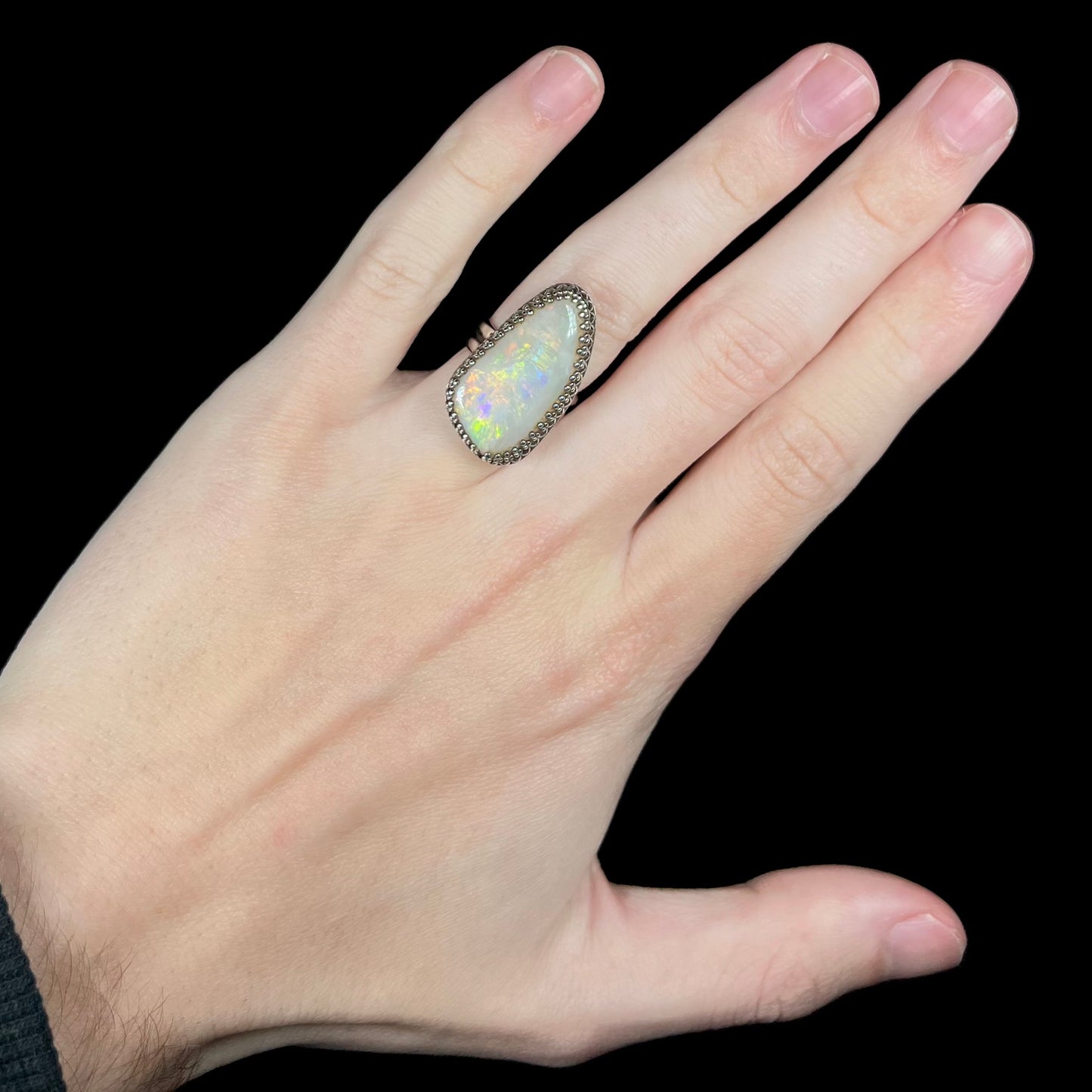 A large, natural Australian opal cocktail ring in sterling silver shown worn on a hand against black background under studio lighting.