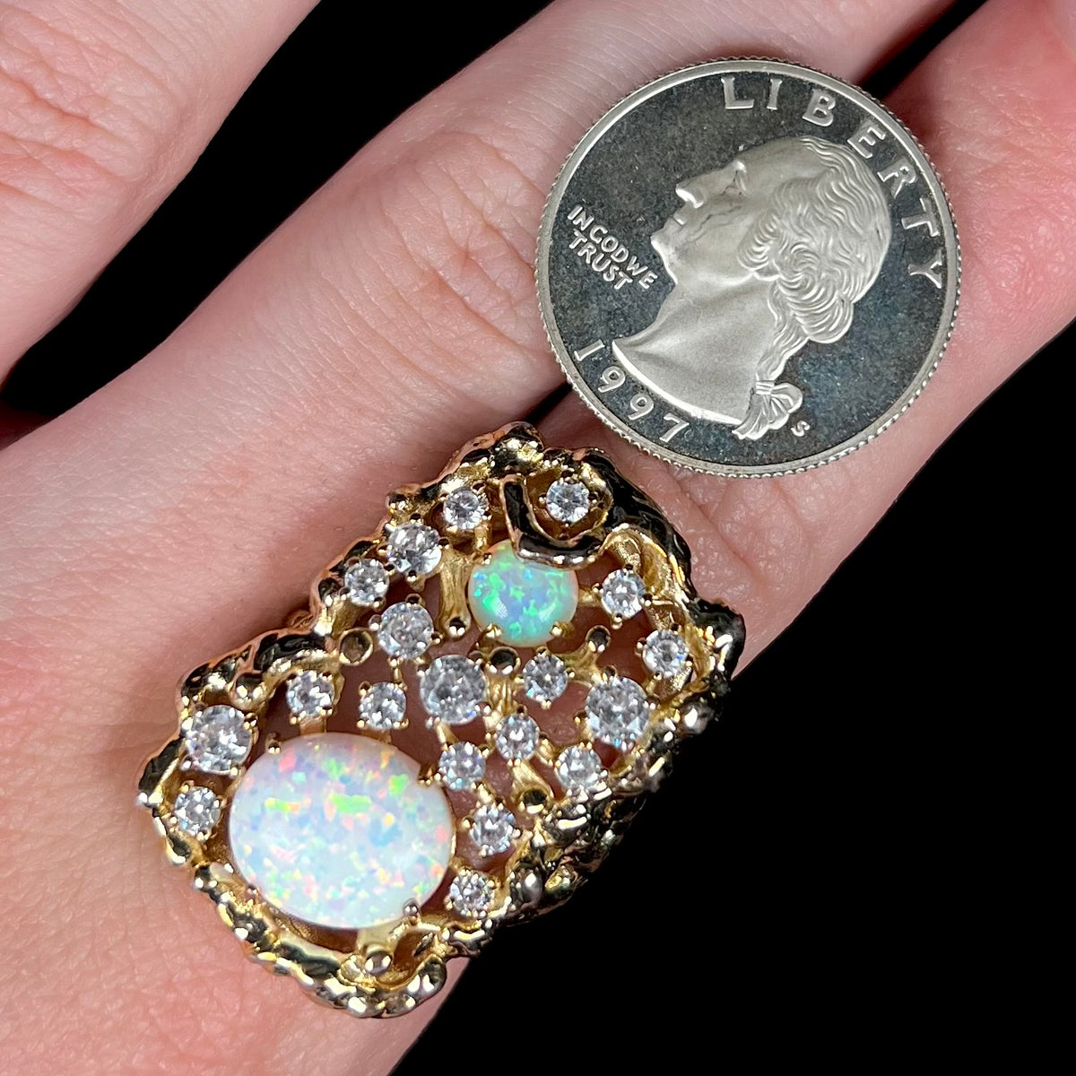 A large lab-created opal and CZ men's ring worn on a finger next to a US quarter coin for scale.