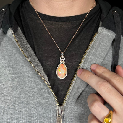 A large pear shaped Ethiopian opal and diamond halo necklace by Le Vian, worn around a model's neck inside of an unzipped hoodie.  The opal has red fire.