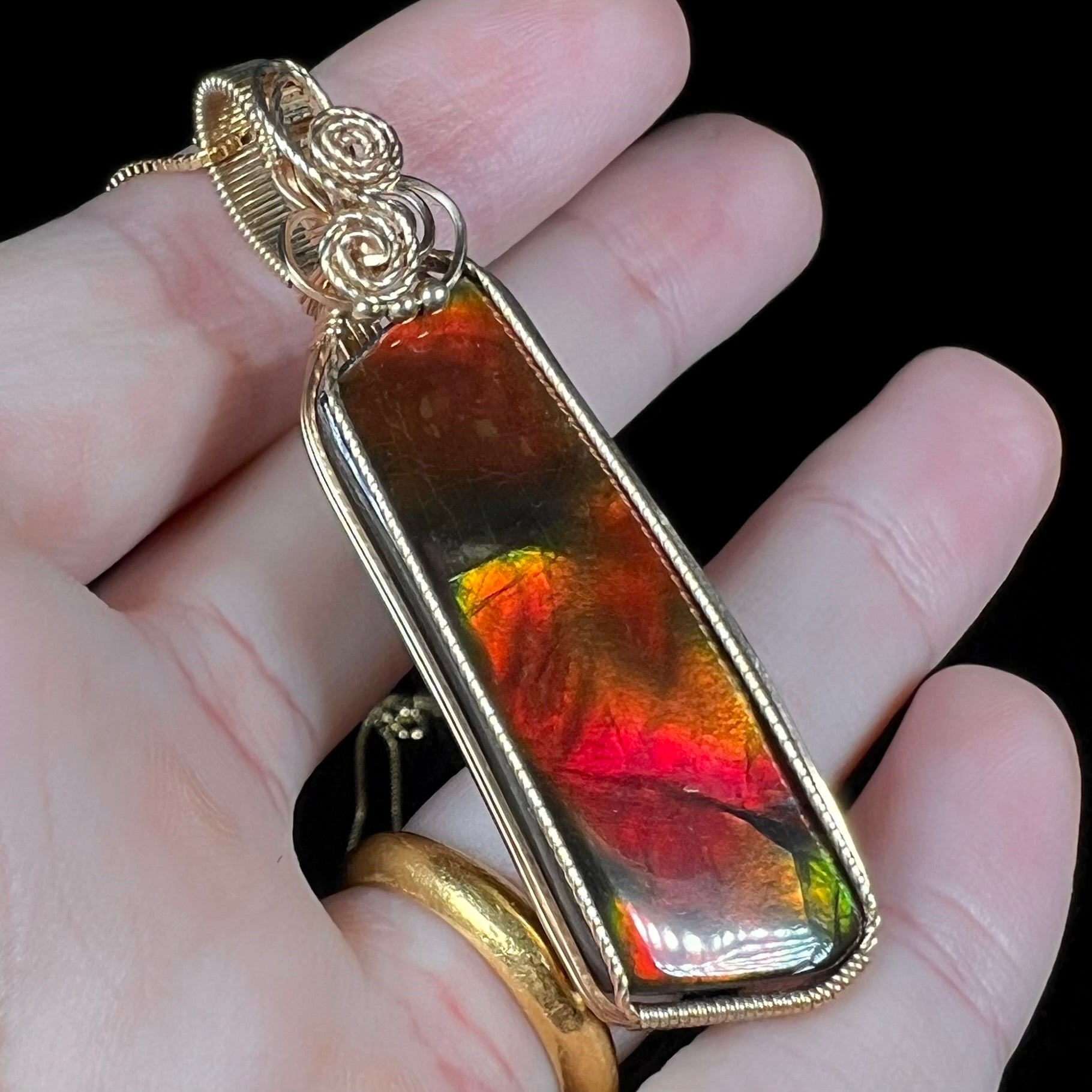 A large red ammolite pendant held at an angle in a hand against a black background.