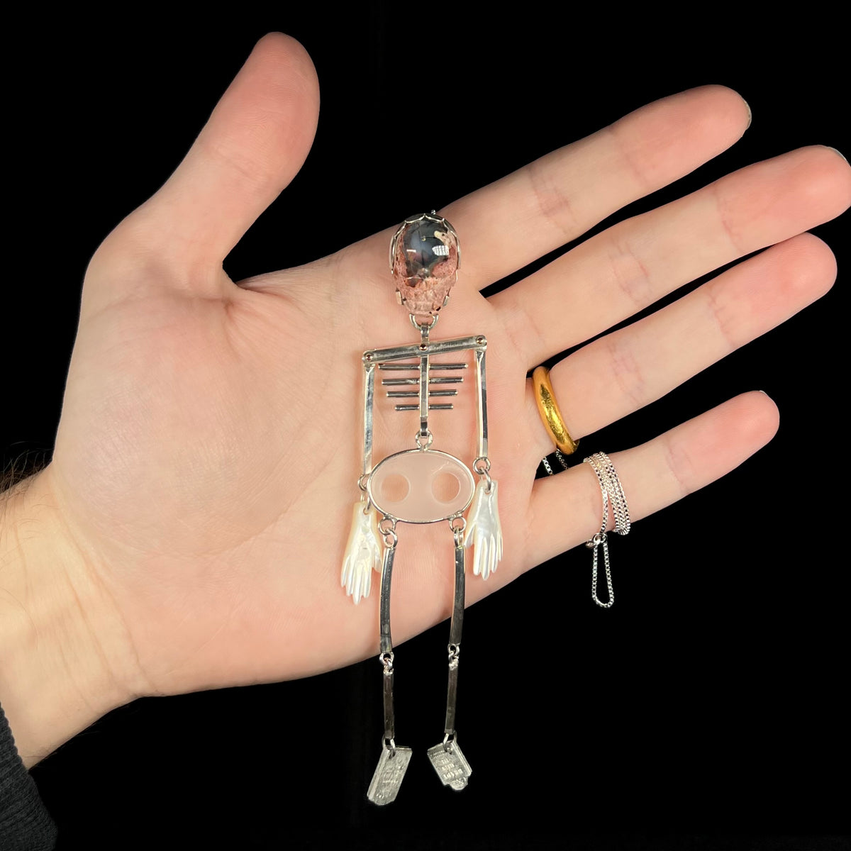 Hand holding a large sterling silver skeleton pendant with cantera matrix opal skull against black background
