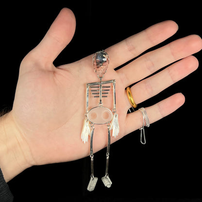 Hand holding a large sterling silver skeleton pendant with cantera matrix opal skull against black background