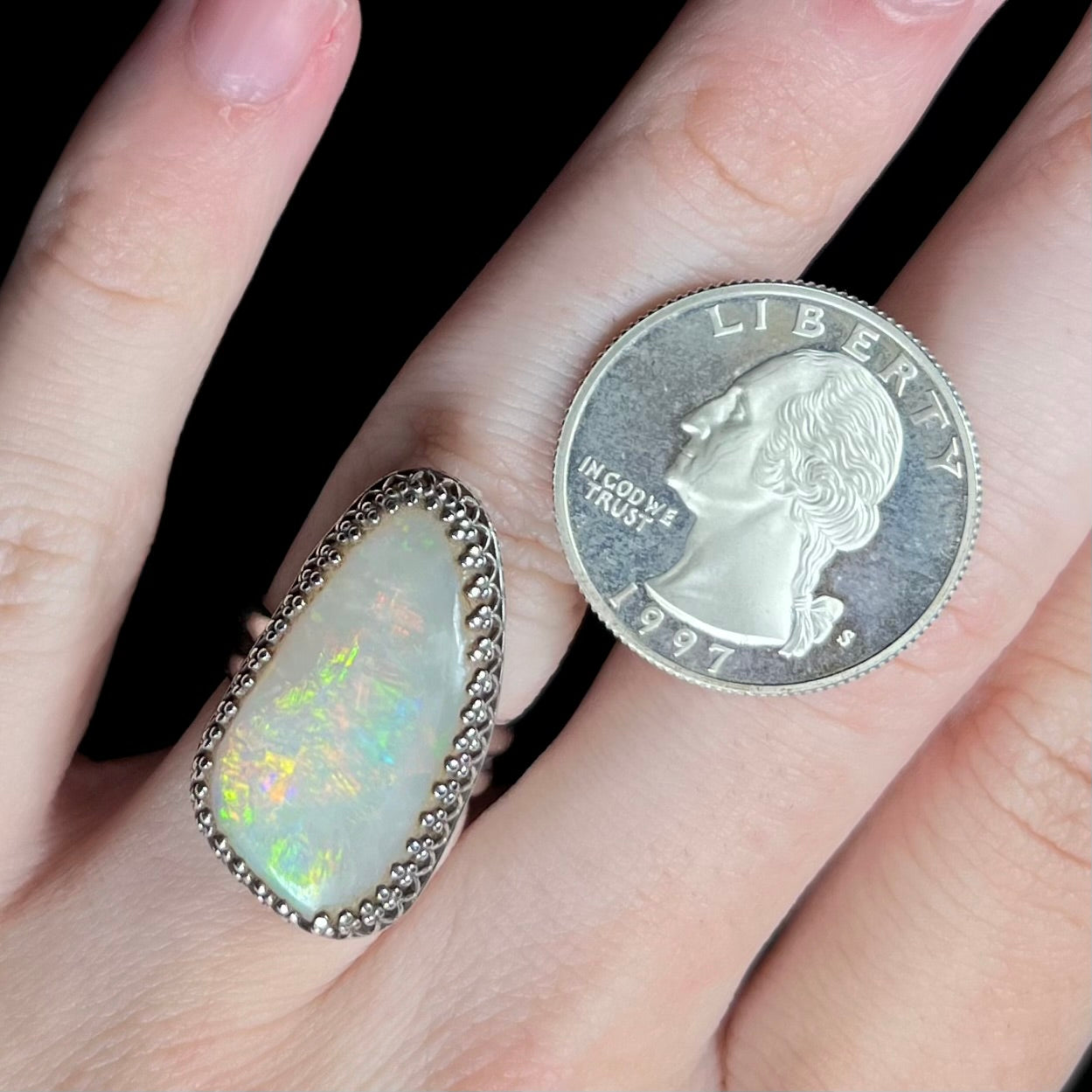 A large sterling silver Australian opal solitaire ring with a regal crown design, worn on a hand next to a US quarter coin for scale.