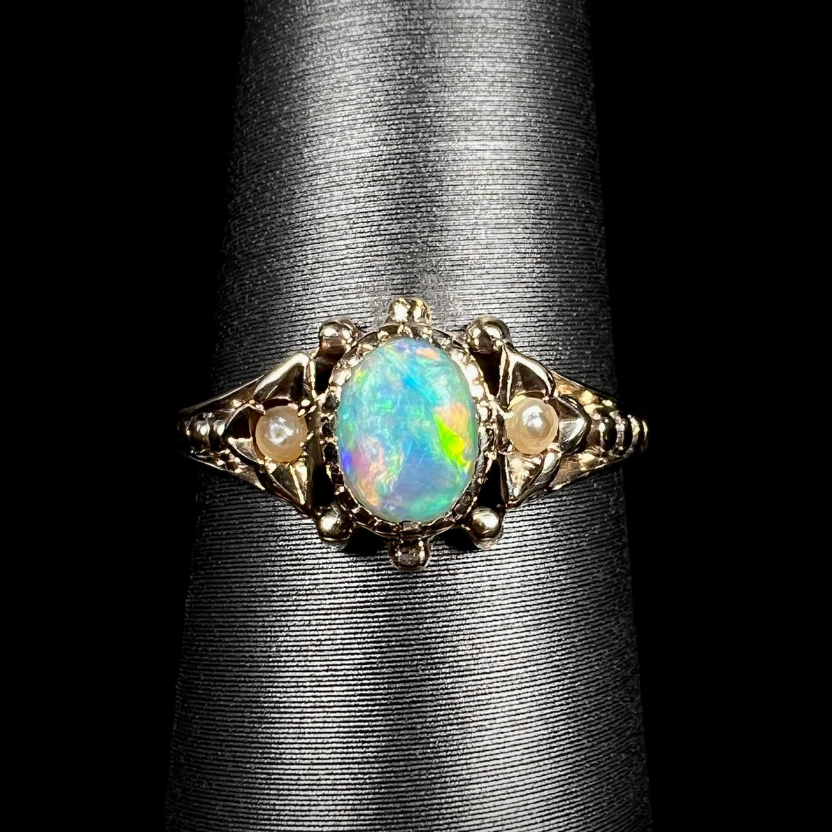 Close-up macro of late Victorian era 9k gold opal and seed pearl engagement ring on ring display