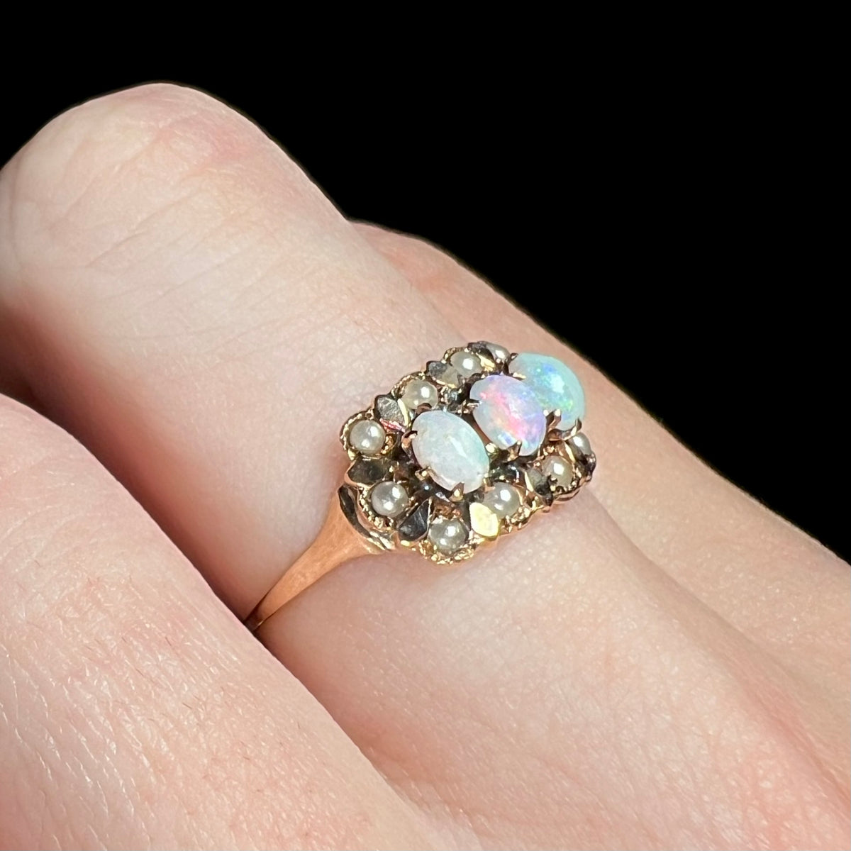 Macro view of a late Victorian era three-stone opal ring with seed pearl accents, worn on finger and shown from angle