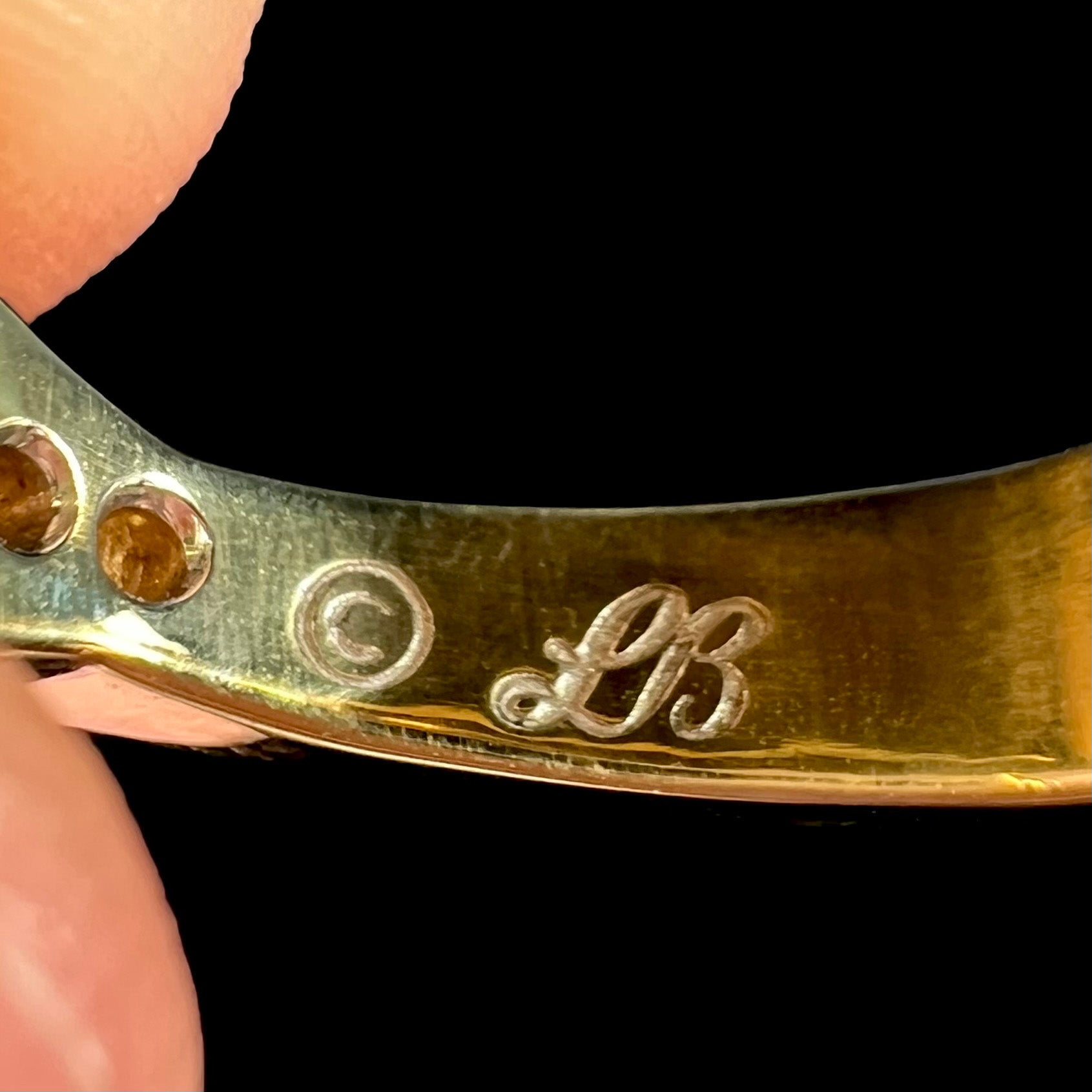 Macro view of the inside of an 18k gold ring's shank showing the hallmark of a cursive "LB" by artist Luciano Bortone.