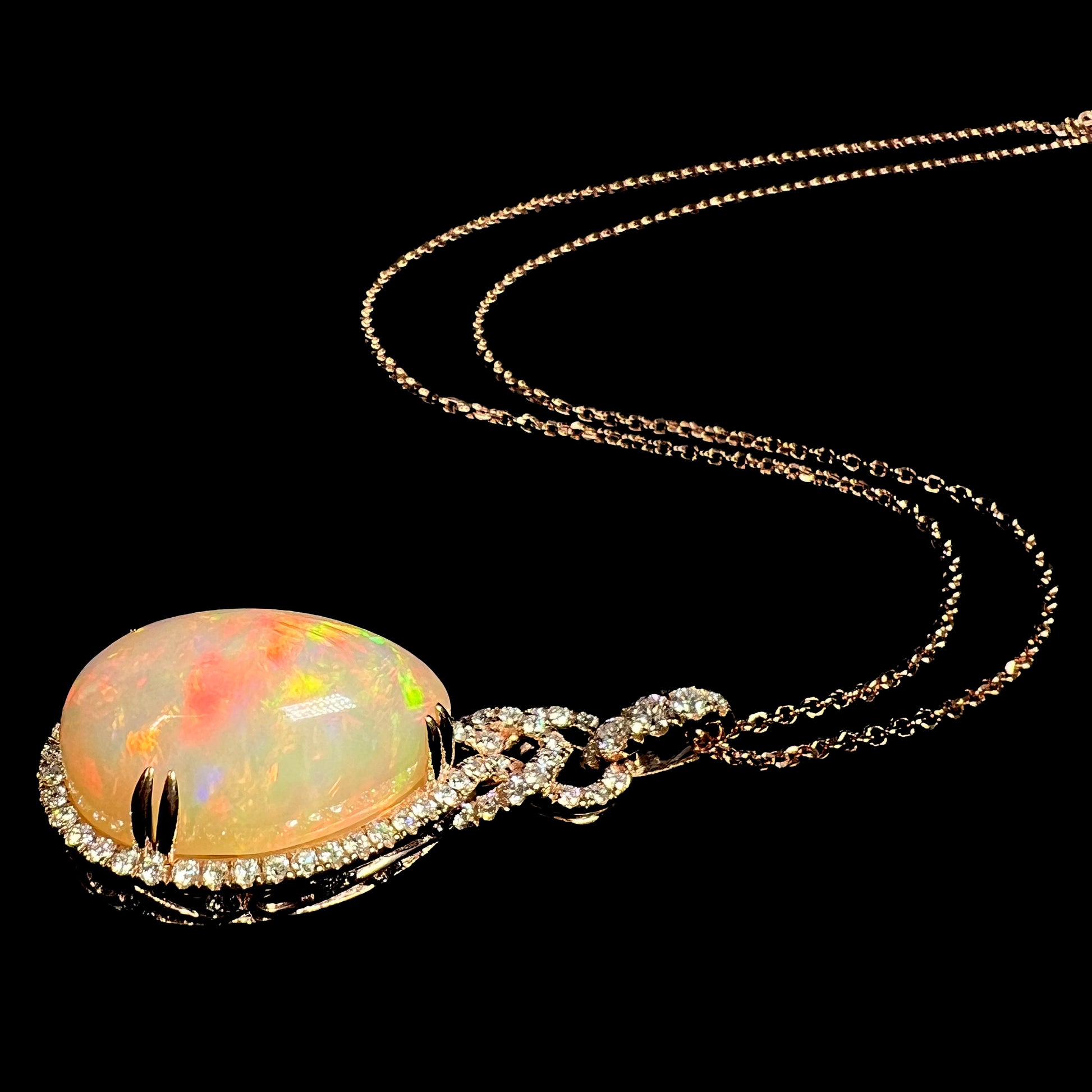 Angled view of a Le Vian rose gold opal and diamond halo necklace shown laying against a black background under LED studio lights.