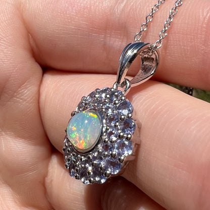 Angled close-up of a sterling silver opal pendant with a light blue tanzanite halo, shown in sunlight close-up.