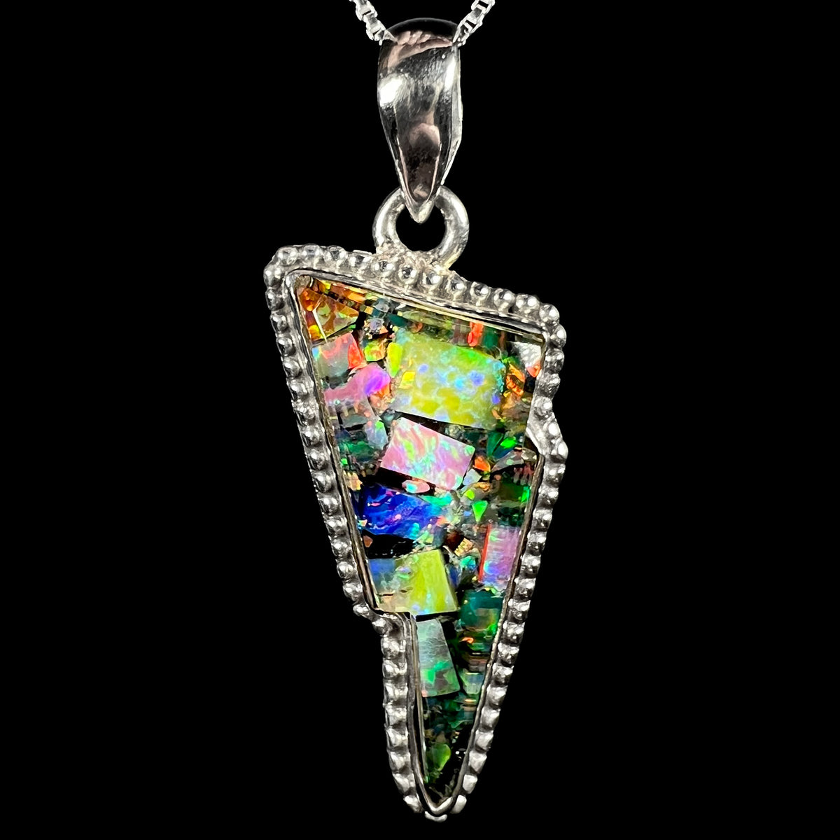 Macro close-up of unisex sterling silver lightning bolt pendant inlaid with lab-created opal mosaic, shown on chain against black background.