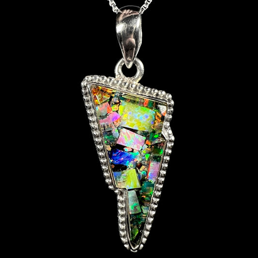 Macro close-up of unisex sterling silver lightning bolt pendant inlaid with lab-created opal mosaic, shown on chain against black background.