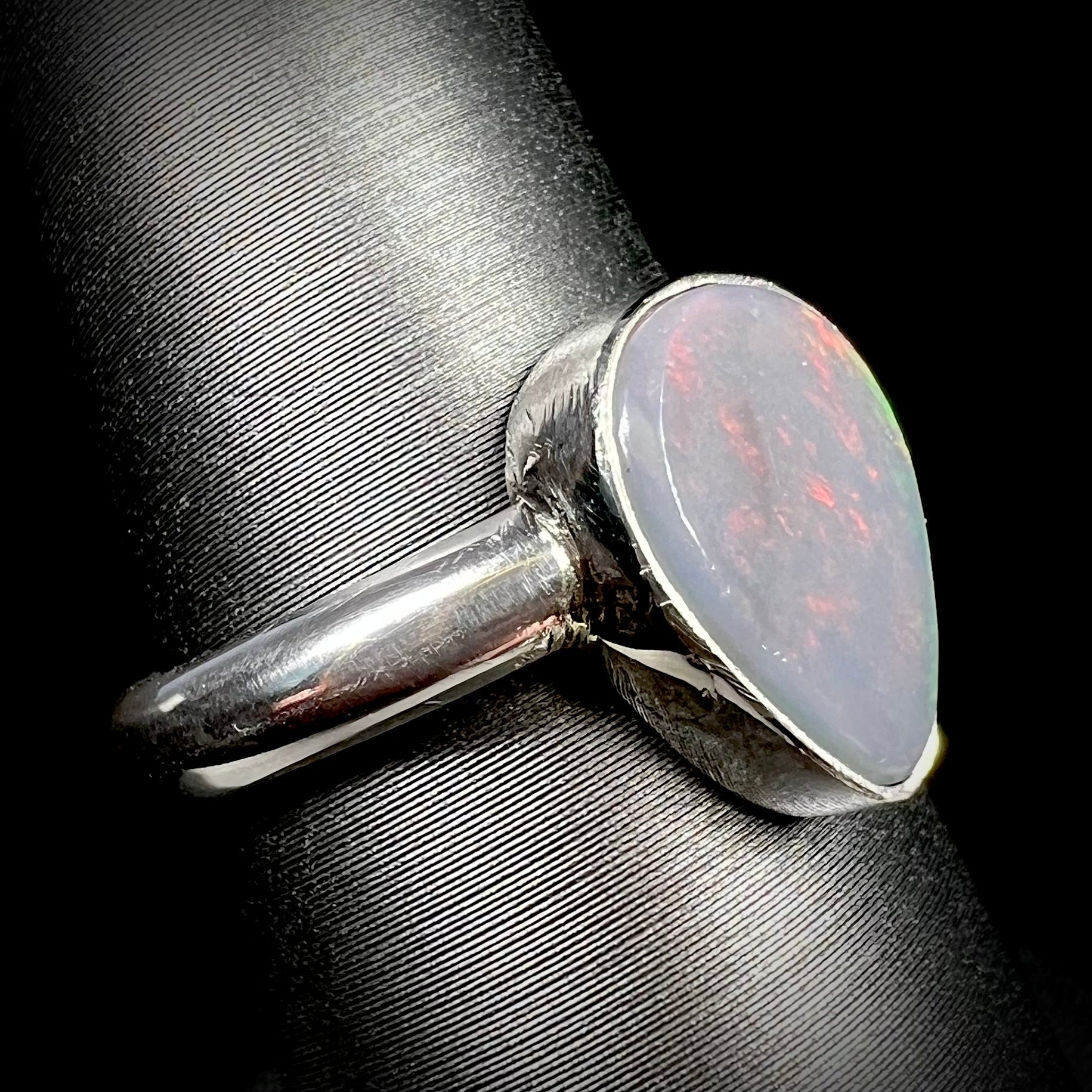 A Lightning Ridge, Australian dark opal ring in sterling silver shown close-up from angle on ring display.  Its N6 body tone is apparent, subtle red play of color is barely visible.