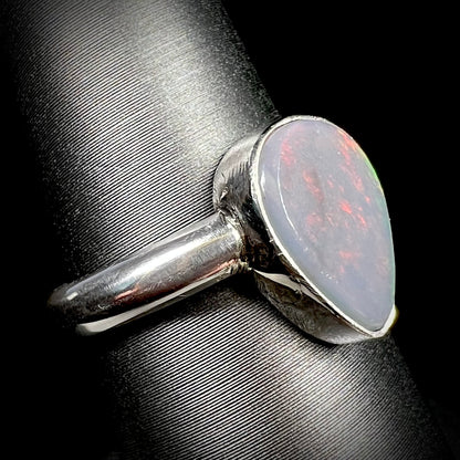A Lightning Ridge, Australian dark opal ring in sterling silver shown close-up from angle on ring display.  Its N6 body tone is apparent, subtle red play of color is barely visible.