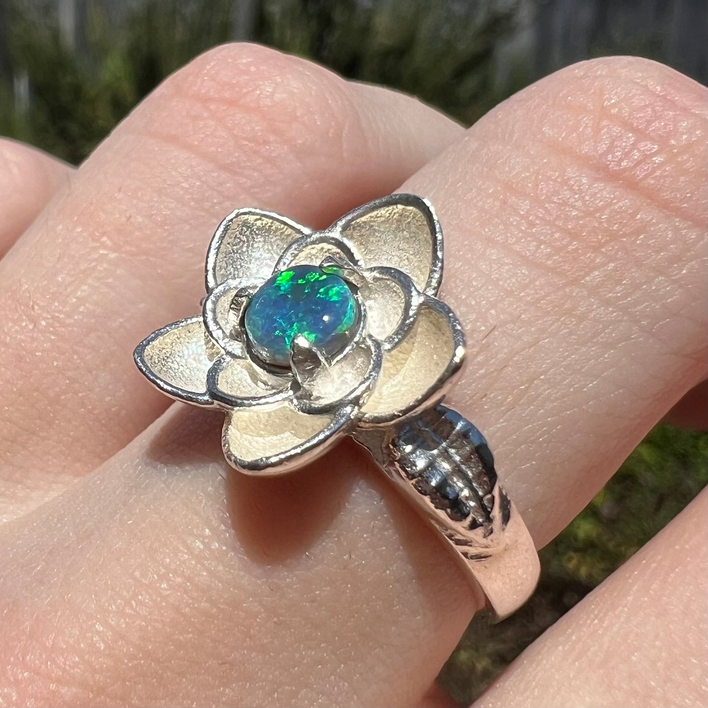 Lightning Ridge black opal ring with silver flower design, shown on finger in natural light